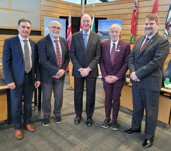 Five men standing in front of banners and flags following a funding announcement