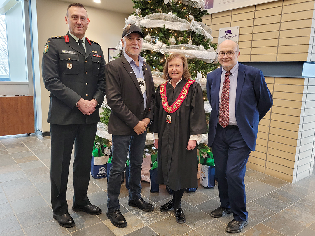 four people standing in front of a Christmas tree