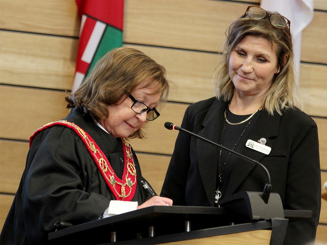 two woman at a podium, the woman on the left signing and the one on the right looking on