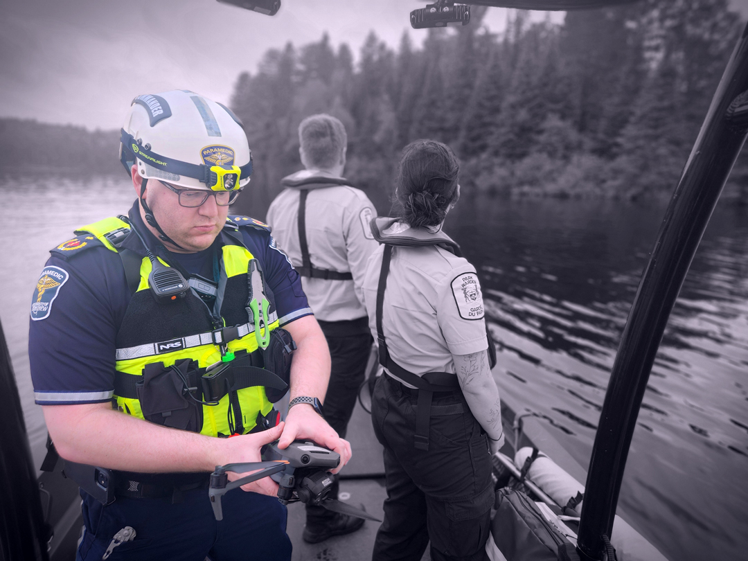 paramedic looking at a piece of equipment and two park wardens in the background looking back at the lake from the boat
