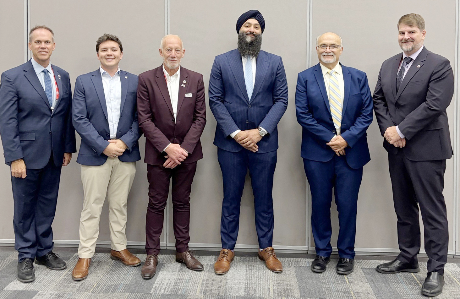 group of six men standing in a row in front of a wall in a boardroom
