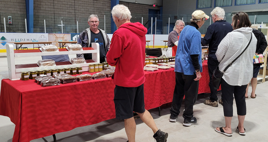 vendor market table inside an arena with customers in front of the table, backs to the camera