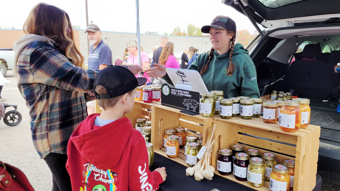 owner of a farm stand on the right speaking with customers at an outdoor market