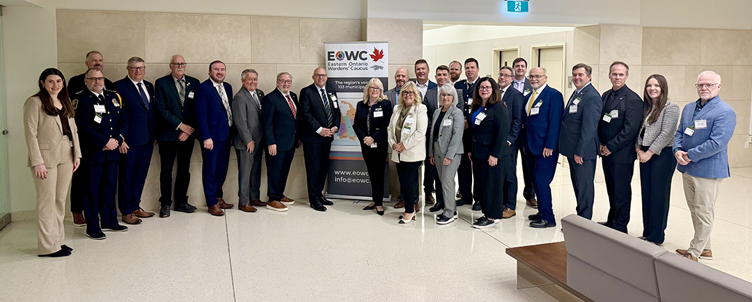large group photo of 25 people with the Eastern Ontario Warden's Caucus banner in the middle behind members of the group