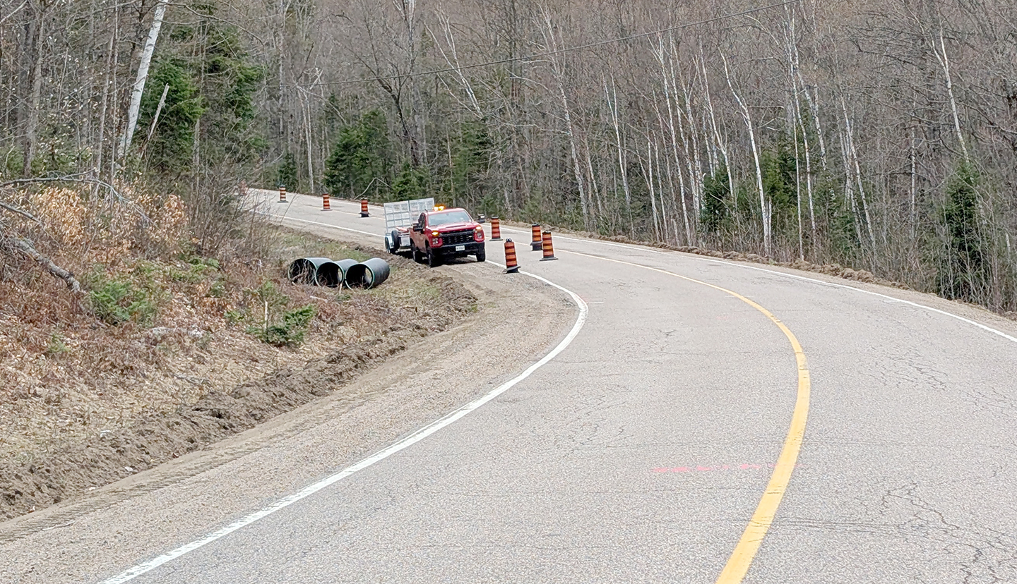 Pre-construction photo curve in the road with culverts on the left side, a truck behind and large construction cones