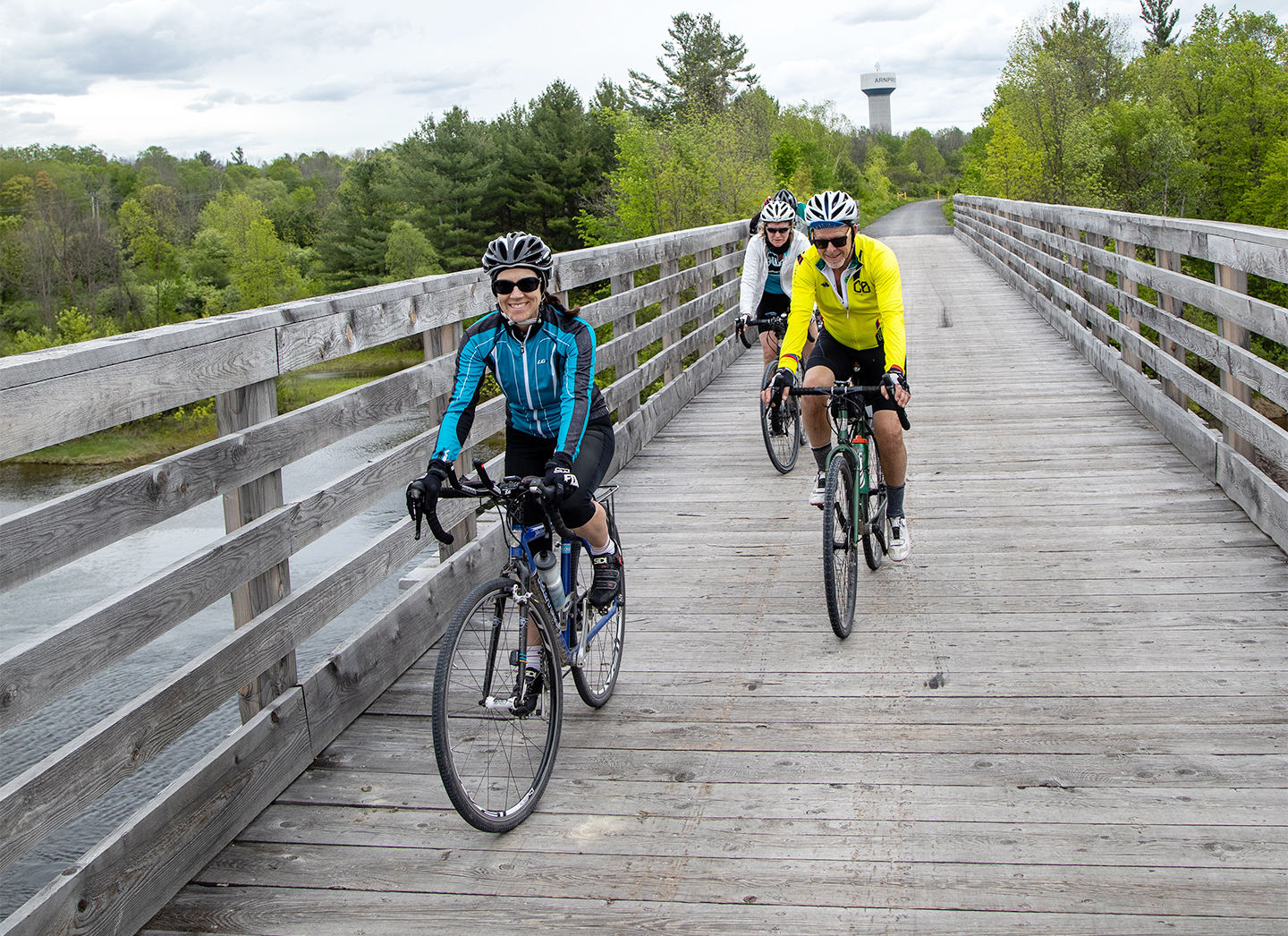 three people cycling across a wooden bridge