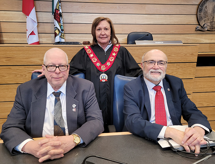 photo of three people with two sitting at a desk and a person standing between them in front of the County of Renfrew logo